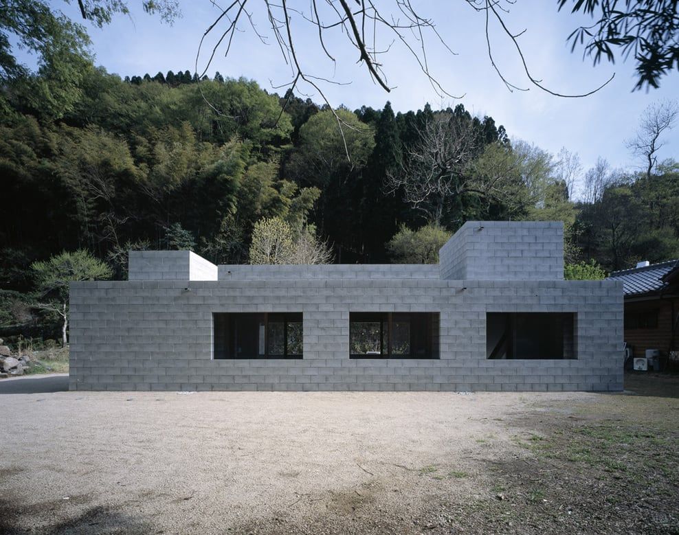 Photo of a house under construction with light gray block walls, against a backdrop of a house with trees.